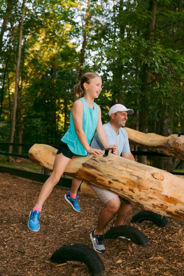 kid and adult at rustic acres rv park. little girl sitting on a log smiling